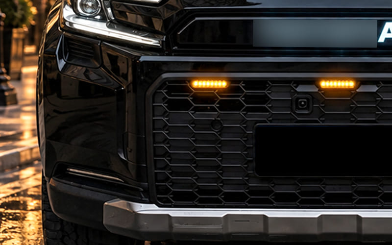 Close view of a black SUV grille with lights, camera and surrounding trim