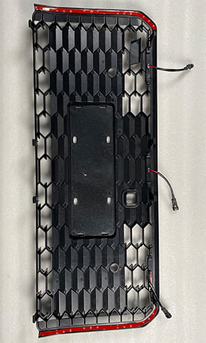 Rear view of a black vehicle grille showing its wiring and mounting structure